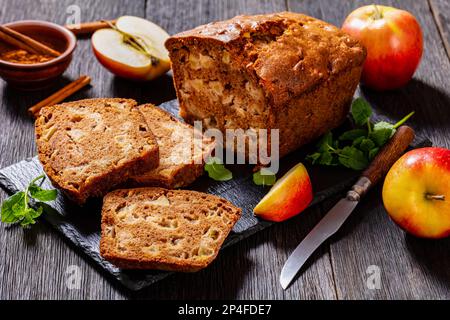 Apfelzimtbrot auf Schieferbrett mit Messer, frische Minze, Apfel und brauner Zucker auf dunklem Holztisch, horizontale Sicht von oben Stockfoto