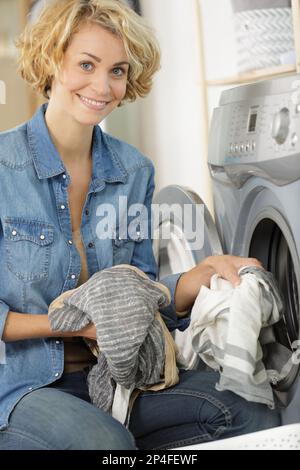 Junge Frau, die Wäsche in die Waschmaschine lädt Stockfoto