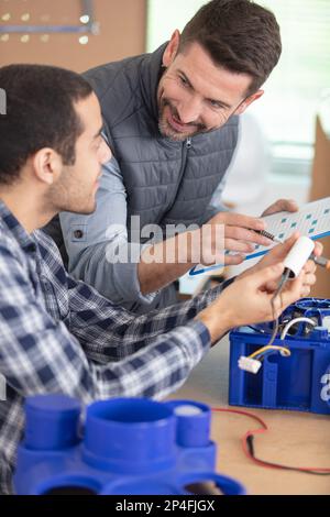 Der Auszubildende in der Werkstatt baut mit seinem Mentor ein Belüftungssystem zusammen Stockfoto