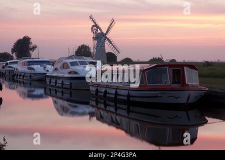 Vergnügungsboote in der Nähe der Windpumpe bei Sonnenuntergang, Thurne Windpump (Morsemühle), Thurne Dyke, Fluss Thurne, The Broads N.P., Norfolk, England Stockfoto