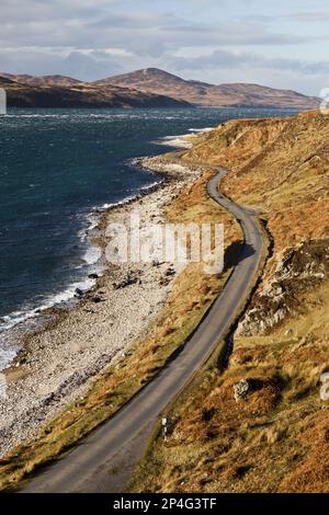 Blick auf die Küste mit der einzigen Straße auf der Insel, die in Richtung Feolin führt, Blick auf Sound of Islay mit Islay und Sgarbh Breac Gipfel Stockfoto