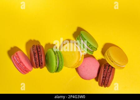 Leuchtend bunte (gelb, rosa, grün, braun) verschiedene Geschmack Macarons süße Kekse auf hohem farbigen Hintergrund. Stapel kleiner französischer Macaronkuchen, Co Stockfoto