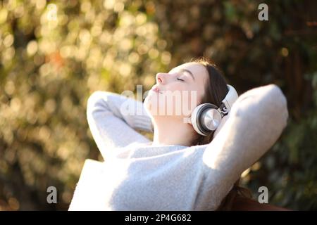 Eine Frau, die sich ausruht und Musik hört, sitzt auf einer Bank in einem Park Stockfoto