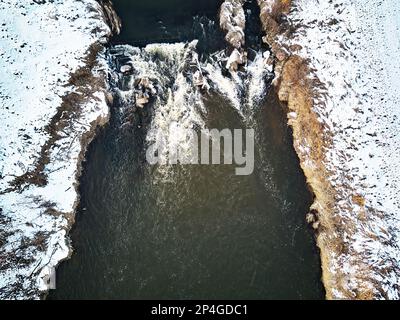 Wasserfall auf dem Winterbach. Schnee an gefrorenen Flussufern. Blick Aus Der Vogelperspektive Auf Den Fluss Cascade. Wasserströmung zwischen Felsen. Europa Stockfoto