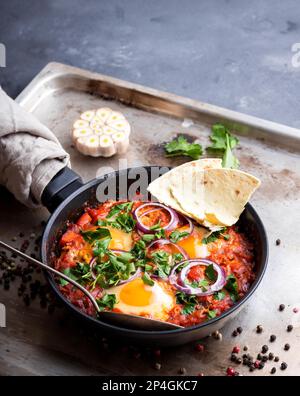 Shakshuka mit Pita-Brot in einer Pfanne. Traditionelles Gericht aus dem Mittleren Osten. Spiegeleier mit Tomaten, Paprika, Gemüse und Kräutern. Shakshouka auf A Stockfoto
