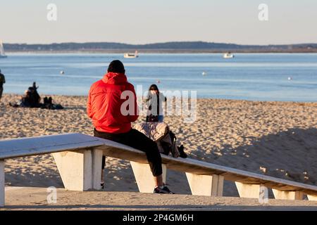 Ein junger Mann, der auf einer Bank sitzt, blickt aufs Meer Stockfoto