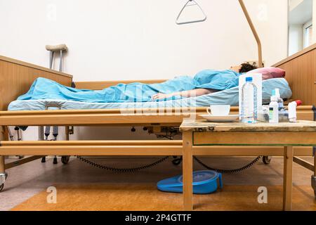 Seitenansicht von Homecare verstellbares elektrisches Krankenhausbett mit Kranken und Tisch mit Medizin zu Hause Stockfoto