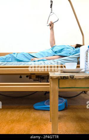 Seitenansicht des elektrischen Krankenhausbetts des Homecare mit kranker Person, die den Griff zu Hause hält Stockfoto