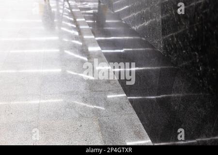 Reflexion der Beleuchtung in grauen und schwarzen Bodenfliesen im Untergrunddurchgang der U-Bahn-Station Stockfoto