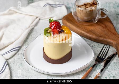 Schokolade und Obstkuchen. Backwaren. Schokoladenkuchen auf grauem Hintergrund. Kuchen mit Erdbeere, Kiwi, Himbeere, Birne und Pfirsich Stockfoto