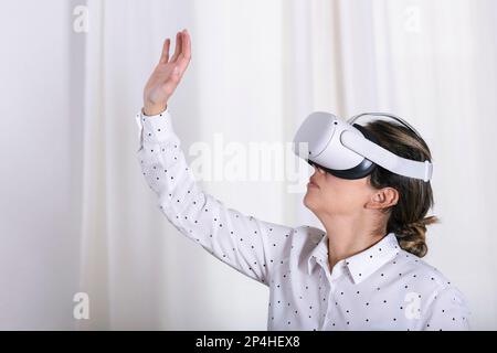 Junge Frau, die im Zimmer sitzt und eine VR-Brille oder eine Brille testet. Stockfoto