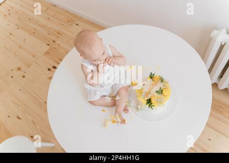 Das kleine Mädchen isst Geburtstagskuchen mit Händen und Beinen Stockfoto