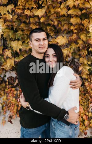 Ein Mann und eine Frau in Pullover und Jeans umarmen einen gelben Busch Stockfoto