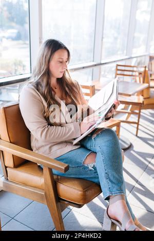 Weiße Frau mit Blazer, die auf ein Notizbuch schaut, sitzt im Café Stockfoto