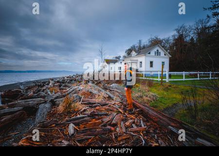 Ein Mann steht auf Baumstämmen in der Nähe des Puget Sound und eines historischen Gebäudes Stockfoto
