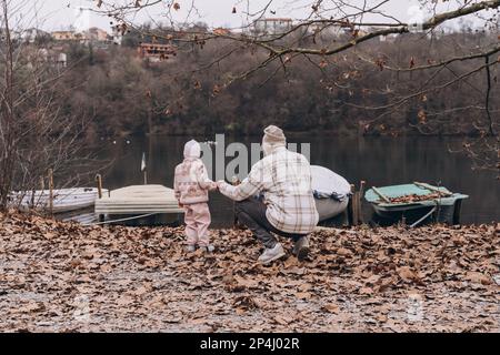 Ein Mann und ein kleines Mädchen schauen sich die Boote im Wasser an, Rückansicht Stockfoto