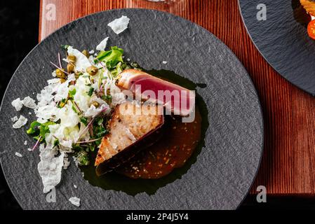Gegrilltes Thunfischsteak mit Sauce auf einem Teller auf einem Holztisch Stockfoto