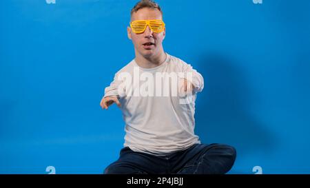 Ein Mann mit stilvoller gelber Brille sitzt auf einem isolierten blauen Hintergrund. Stockfoto