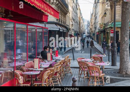 Ein Mann sitzt vor der Brasserie de l'Isle Saint-Louis Rue Saint-Louis en Ille erstreckt sich im Hintergrund, Paris. Stockfoto
