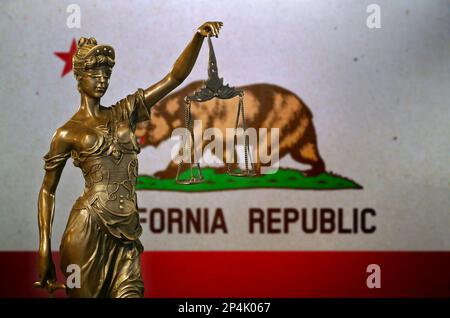 Nahaufnahme einer kleinen Bronzestatuette von Lady Justice vor einer kalifornischen Flagge. Stockfoto