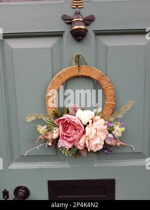 Ein saisonaler Kranz aus rosa Rosen auf einer grauen holzgetäfelten Tür. Stockfoto