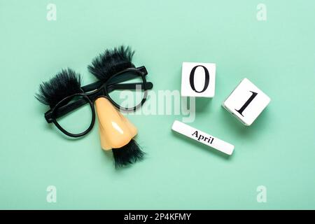 Lustiges Gesicht - gefälschte Brille, Nase und Schnurrbart, Kalender mit Datum 01. April auf grünem Hintergrund Happy Fools Day Konzept 1. April Party Feiertagsgrüße Stockfoto