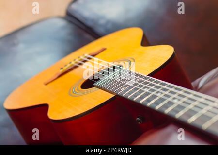 Eine Nahaufnahme der klassischen Akustikgitarre mit Nylonschnüren, die auf einer Couch liegt. Stockfoto