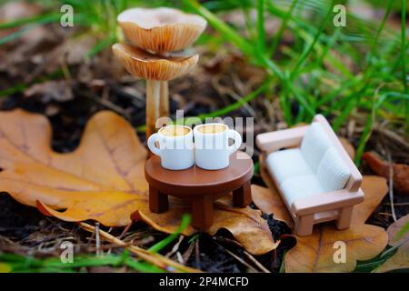 Schönheit der Natur und der Komfort eines gemütlichen Wohnbereichs in einem. Miniaturmöbel und Kaffeetassen, die von frischen Pilzen auf pigmentierten Blättern platziert werden Stockfoto