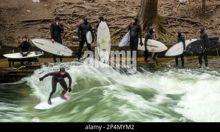 München, Deutschland. 06. März 2023. Surfer stehen bei eisigen Temperaturen mit ihren Boards im Eisbach im Englischen Garten, der sich im Herzen der bayerischen Hauptstadt befindet. Die Eisbach-Welle ist zu jeder Jahreszeit ein echter Hotspot. Kredit: Peter Kneffel/dpa/Alamy Live News Stockfoto