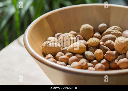 Verschiedene Nüsse in einer großen Holzschüssel auf einem blattgrünen Hintergrund Stockfoto
