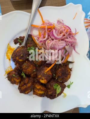 Garnelen, Masala-Braten, serviert auf einem weißen Teller mit einer Seite Zwiebelsalat und Karottensalat. Stockfoto