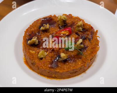 Nahaufnahme einer Schüssel mit frisch zubereitetem Muhammara, serviert in einer weißen Keramikschüssel und garniert mit frischer Walnuss und rotem Pfeffer. Arabisch oder Mittelohr Stockfoto