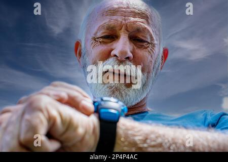 Porträt eines Seniorenmannes, der auf seine Uhr schaut.Seniorensportler überwacht seine Herzfrequenz und seinen Blutdruck mit der Smartwatch am Handgelenk. Stockfoto
