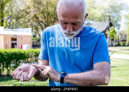 Porträt eines Seniorenmannes, der auf seine Uhr schaut.Seniorensportler überwacht seine Herzfrequenz und seinen Blutdruck mit der Smartwatch am Handgelenk. Stockfoto