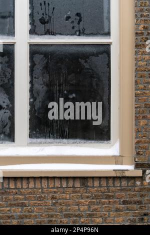 Fassade eines alten holländischen Backsteinhauses in Dordrecht, ein frostiges verschneites holländisches Fenster im Winter, Handabdrücke, Flecken und Kondensation auf dem Glas. Stockfoto