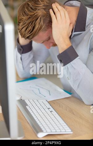 Junger Büroangestellter schockiert von schlechten Nachrichten bei der Arbeit Stockfoto