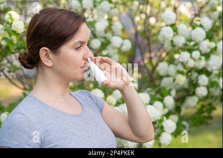 Kaukasische Frau verwendet ein Nasenspray, während sie im Park spazieren geht. Stockfoto