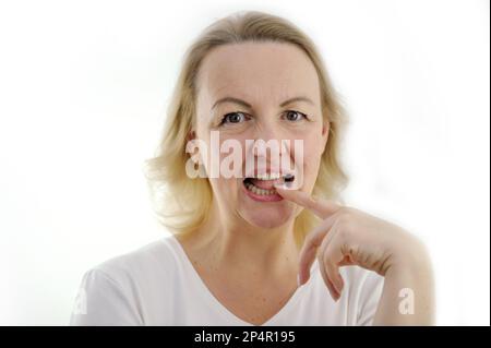 Denk über den Antrag nach, Frau hat Zeigefinger mit geöffneten Zähnen gebissen und in den weißen Hintergrund geschaut. Ein Interessantes Angebot, das sich nur schwer ablehnen lässt. Unterhaltsame Geschichtenkommunikation. Denk an Fokus Stockfoto