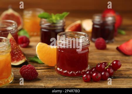 Gläser mit verschiedenen Marmeladen und frischen Zutaten auf einem Holztisch Stockfoto