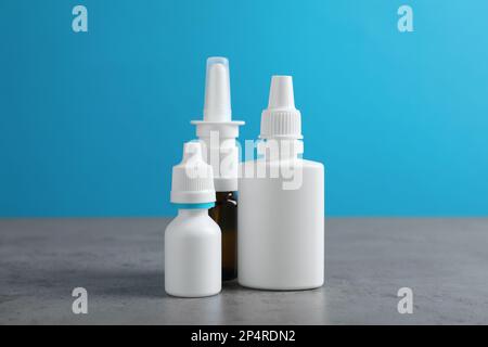 Nasensprays in verschiedenen Flaschen auf grauem Tisch vor hellblauem Hintergrund Stockfoto