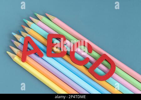 Back-to-School-Konzept mit verschiedenen Buchstaben und Buntstiften in Pastellfarben auf blauem Hintergrund Stockfoto