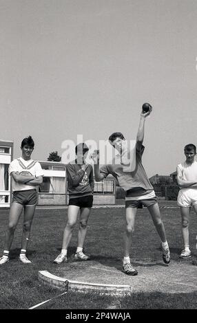 1989, histokal, Sporttag der Sekundarschule, ein Linkshänder, der die Dreharbeiten macht, beobachtet von anderen männlichen Schülern, Sleaford, Lincs, England, Großbritannien. Der Shot Put ist ein athletisches Ereignis, bei dem ein schwerer Kugelball, so weit wie möglich, aus einem kleinen Kreis in England, in Großbritannien, geworfen wird Stockfoto