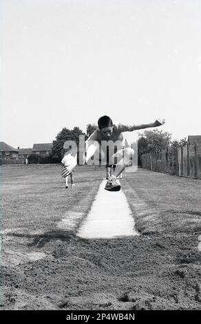 1989, historischer Sporttag der Sekundarschule, Vorderansicht eines männlichen Schülers, der in der Luft in eine Sandgrube springt, England, Großbritannien. Als sportliche Kombination aus Geschwindigkeit, Kraft und Agilität besteht das Ziel des langen Sprungs darin, so weit wie möglich aus der Startposition zu springen. Stockfoto