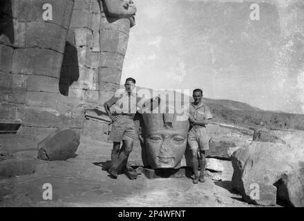 1940er, historisch, zwei britische Soldaten stehen für ein Foto neben einer Statue eines pharaokopfes, an den antiken Ruinen des Tempels von Karnak, Luxor, Ägypten. Die ägyptischen Ruinen von Karnak sind ein antiker Gottesort, der als größte religiöse Stätte der Welt gilt und der Ort sein soll, an dem der gott Amun mit den Menschen der Erde verbunden ist. Stockfoto