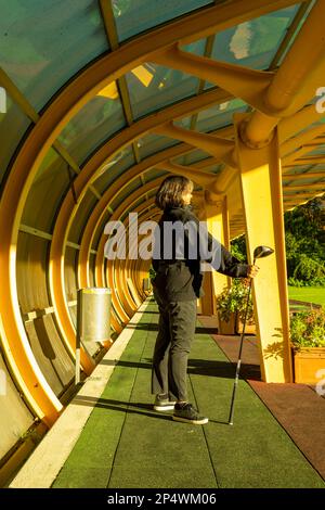 Golfer steht und hält ihren Golfklubfahrer in einem Gebäude auf einer Driving Range auf dem Golfplatz an einem sonnigen Tag in Ascona, Schweiz. Stockfoto