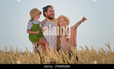 Vater der Mutter einer kaukasischen Familie mit Kind Mädchen Eltern mit Kind Tochter bärtiger Mann und blonde Frau mit Hut im Freien in Weizen goldenes Feld Look Stockfoto