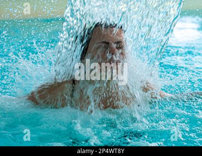 Frauengesicht Entspannen in einem Hydromassage-Pool mit fallendem Wasser in der Schweiz. Stockfoto