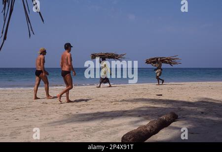 24.02.2008, Thandwe, Rakhine State, Myanmar, Asien - zwei Touristen laufen am Ngapali Beach entlang und treffen Einheimische, die Feuerholz tragen. Stockfoto