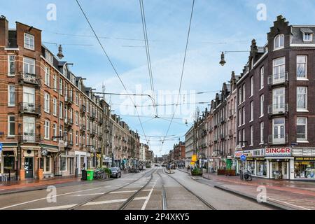 Amsterdam, Niederlande - 10. April 2021: Eine leere Stadtstraße mit Gebäuden und Autos auf beiden Seiten, im mittleren Teil der Straße ist ein blauer Himmel darüber Stockfoto