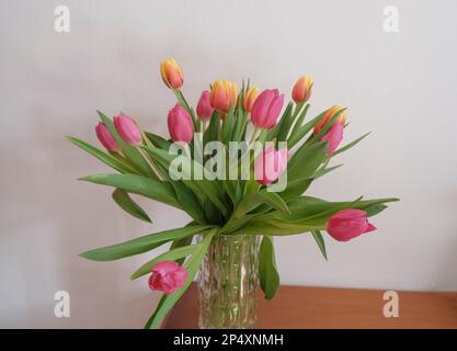 Ein Strauß rosa-gelber Tulpen in Vase, in Weiß, alles auf der Holzschublade. Innenausstattung. Innenansicht des Hotels Stockfoto